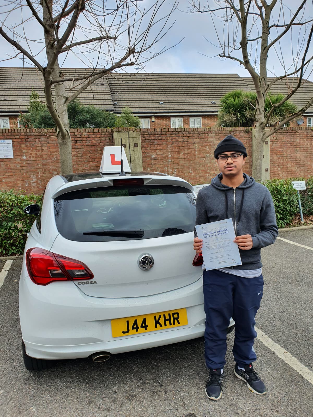 A happy learner holding their driving test pass certificate by the My First Drive car