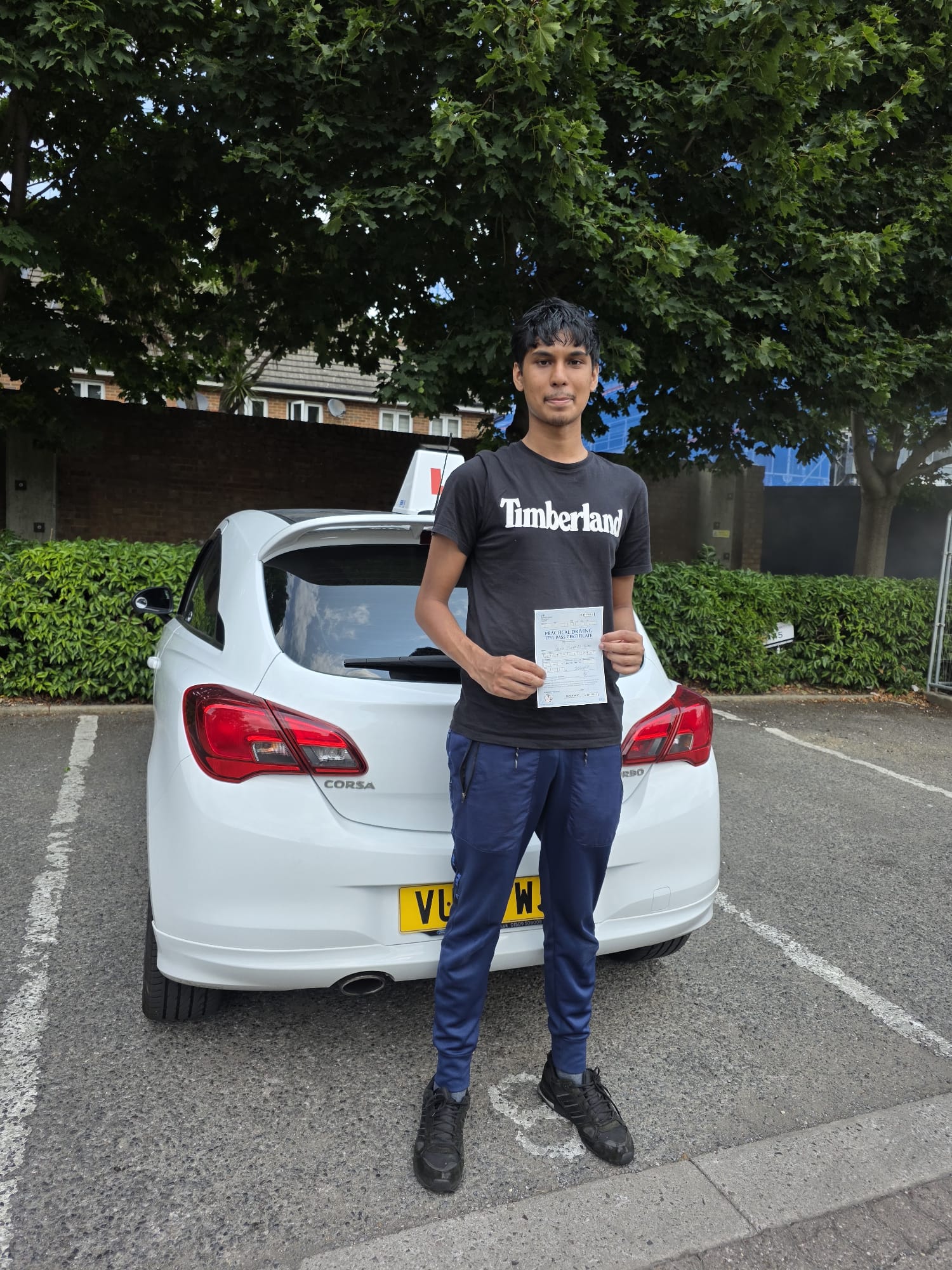 A happy learner holding their driving test pass certificate by the My First Drive car