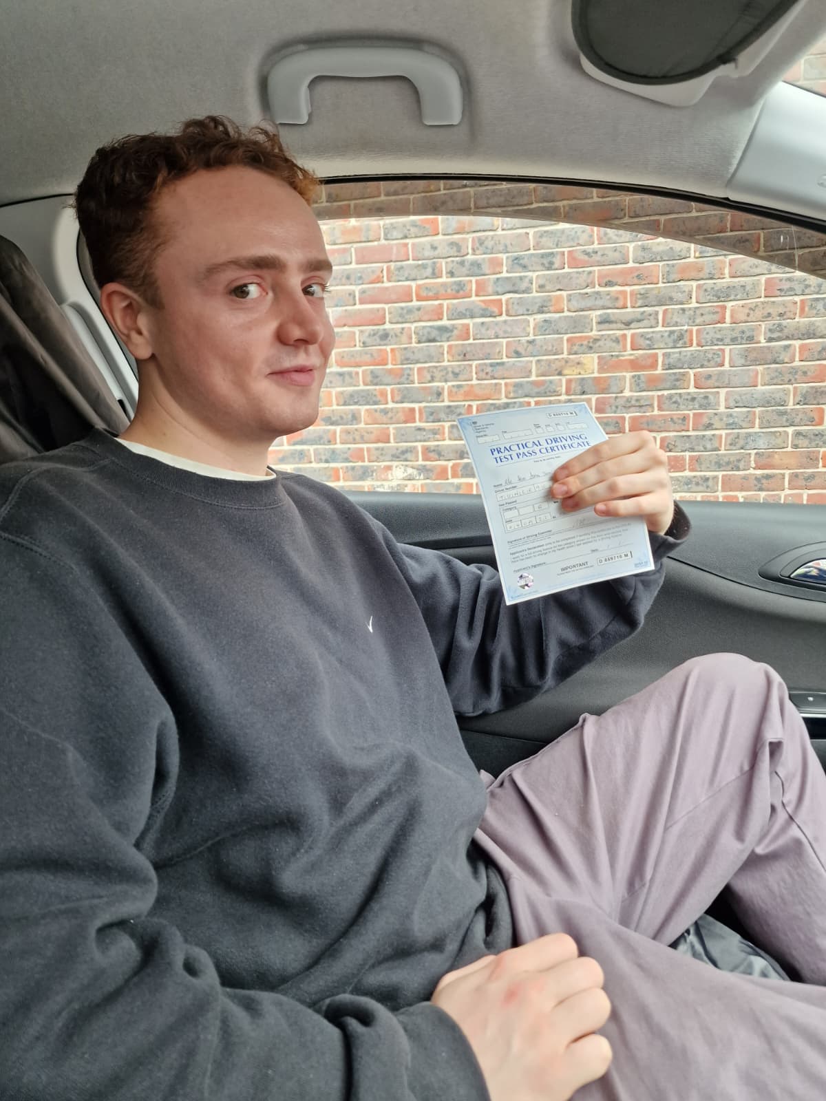 A happy learner holding their driving test pass certificate by the My First Drive car