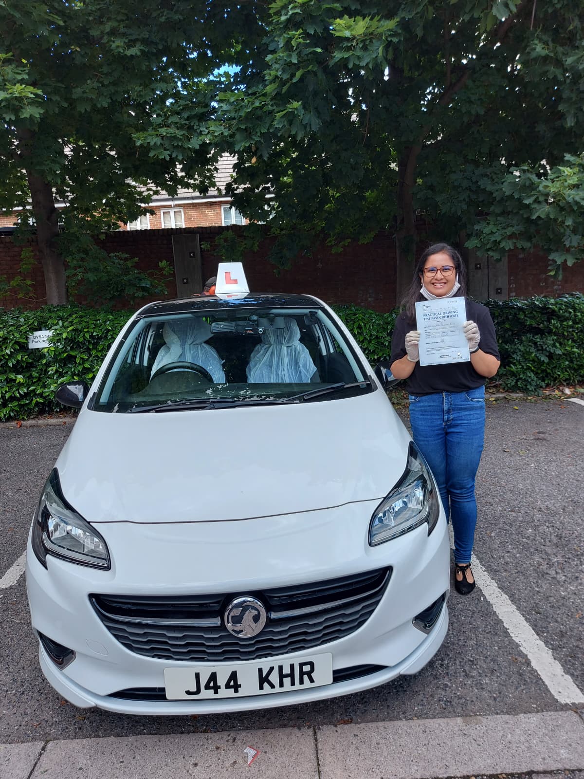 A happy learner holding their driving test pass certificate by the My First Drive car