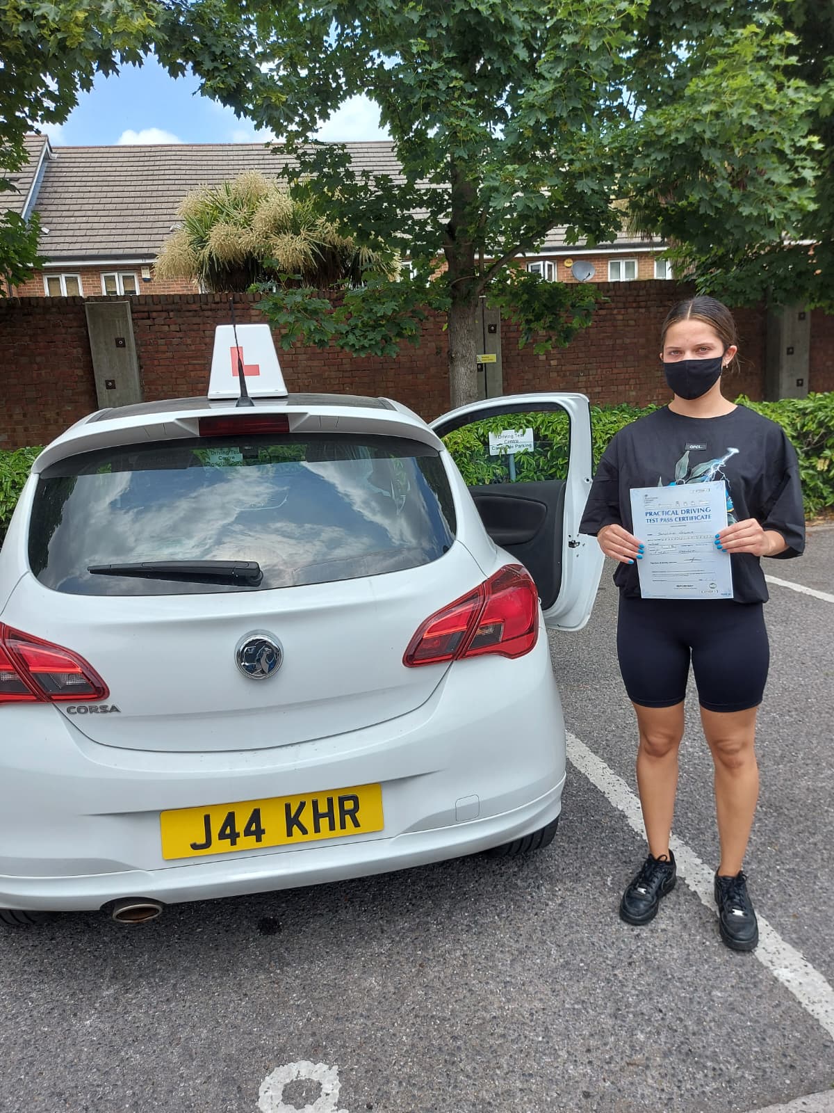 A happy learner holding their driving test pass certificate by the My First Drive car
