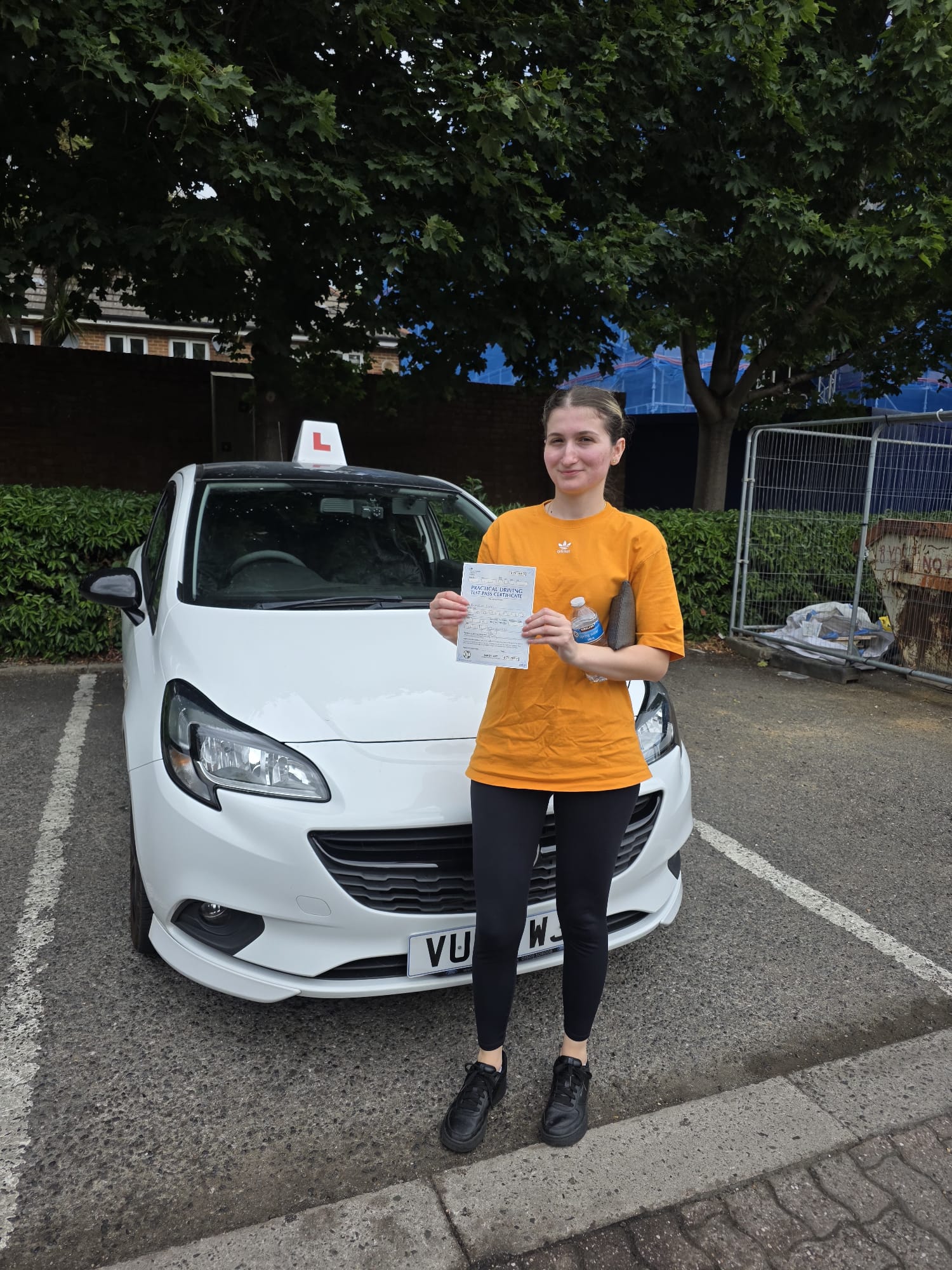 A happy learner holding their driving test pass certificate by the My First Drive car