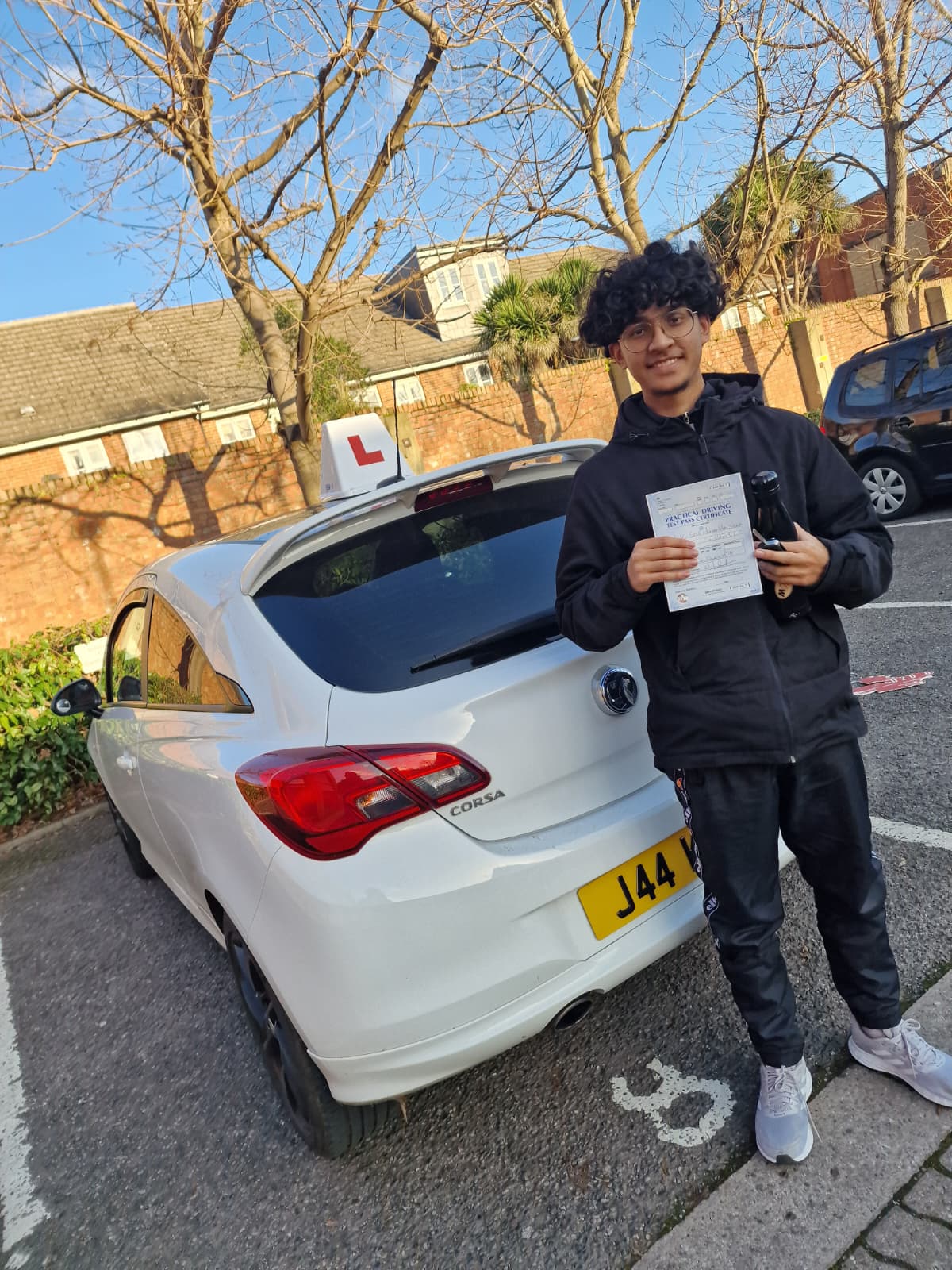 A happy learner holding their driving test pass certificate by the My First Drive car