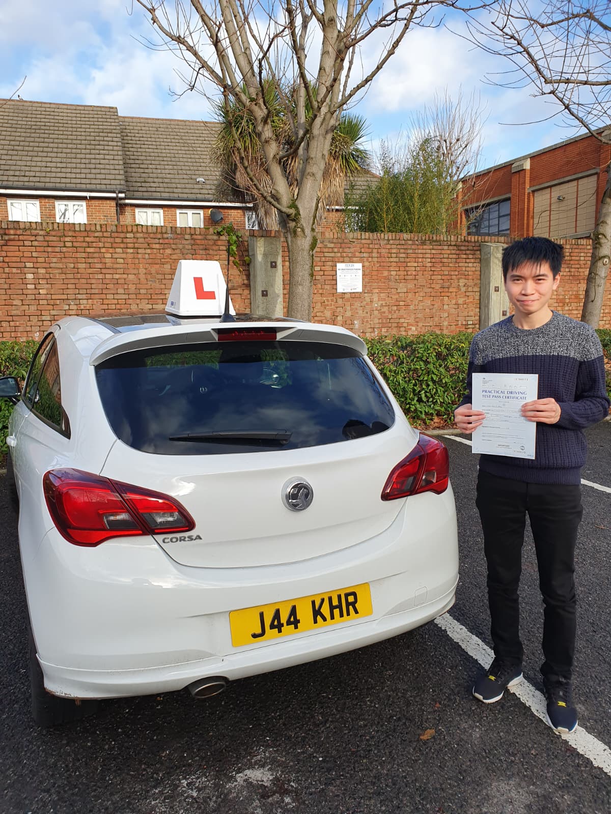 A happy learner holding their driving test pass certificate by the My First Drive car