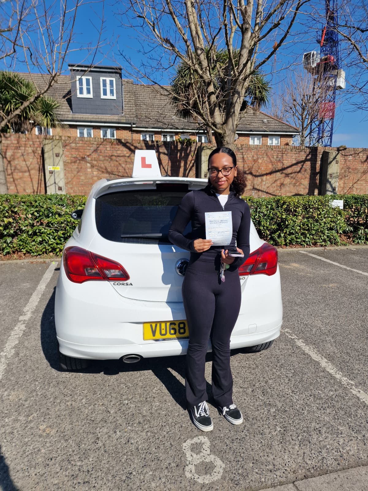 A happy learner holding their driving test pass certificate by the My First Drive car