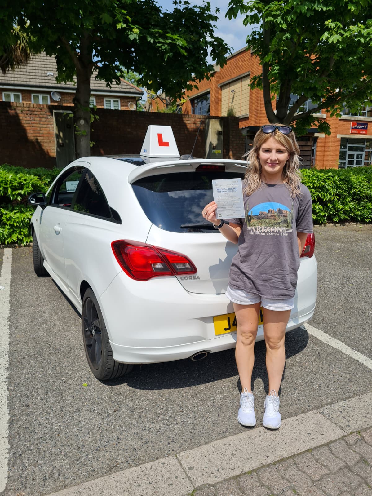 A happy learner holding their driving test pass certificate by the My First Drive car