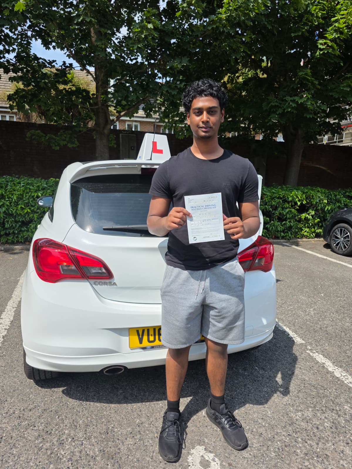 A happy learner holding their driving test pass certificate by the My First Drive car