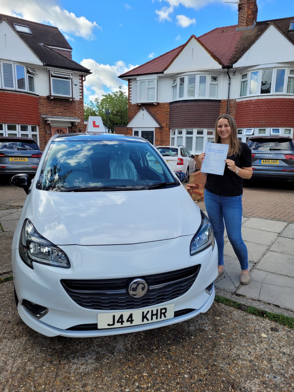 A happy learner holding their driving test pass certificate by the My First Drive car
