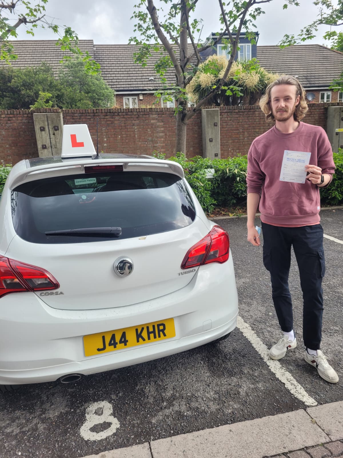 A happy learner holding their driving test pass certificate by the My First Drive car