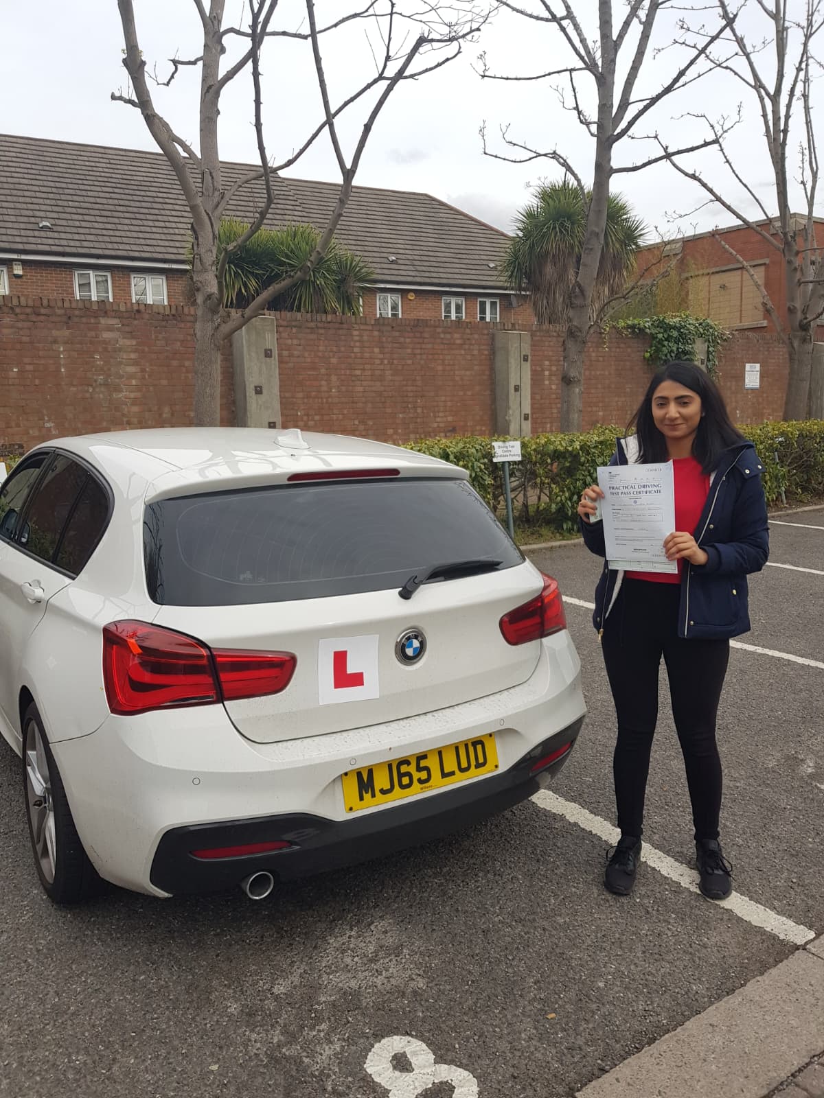 A happy learner holding their driving test pass certificate by the My First Drive car