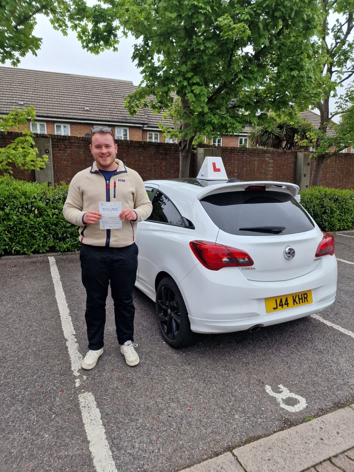 A happy learner holding their driving test pass certificate by the My First Drive car