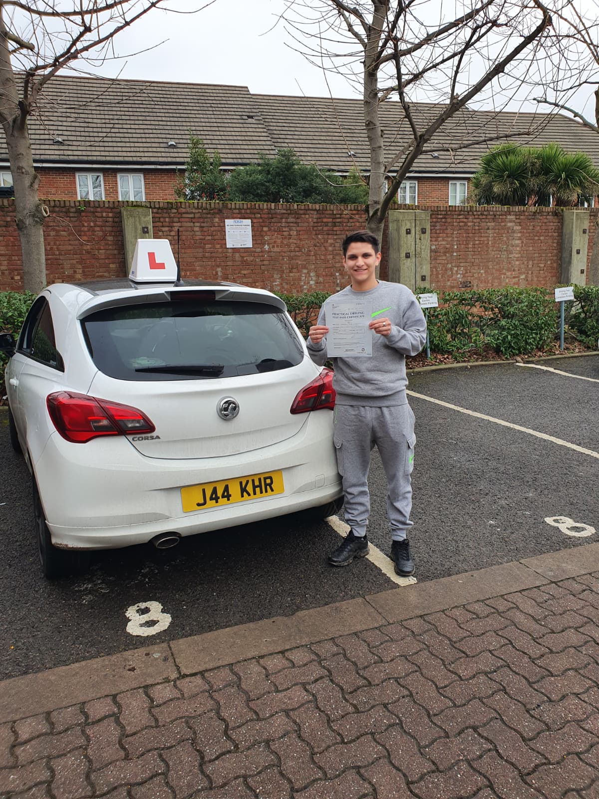 A happy learner holding their driving test pass certificate by the My First Drive car