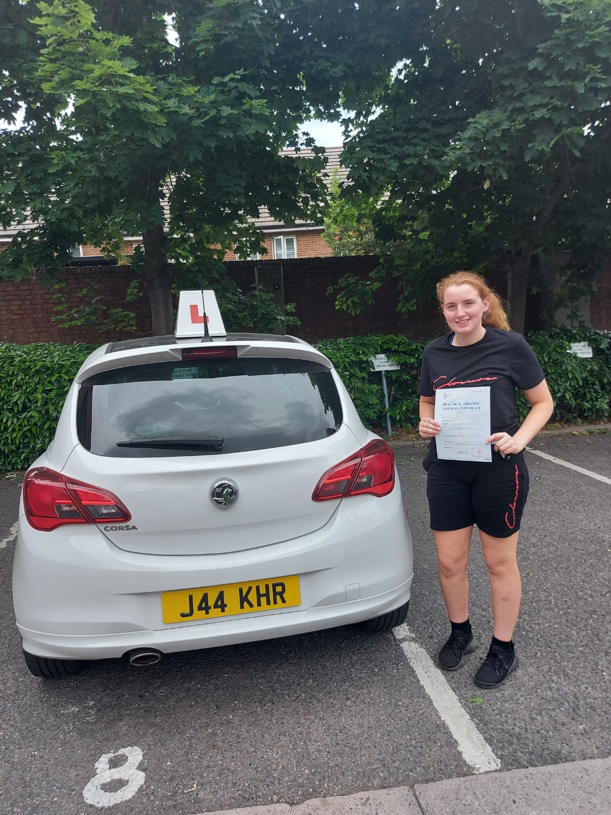 A happy learner holding their driving test pass certificate by the My First Drive car