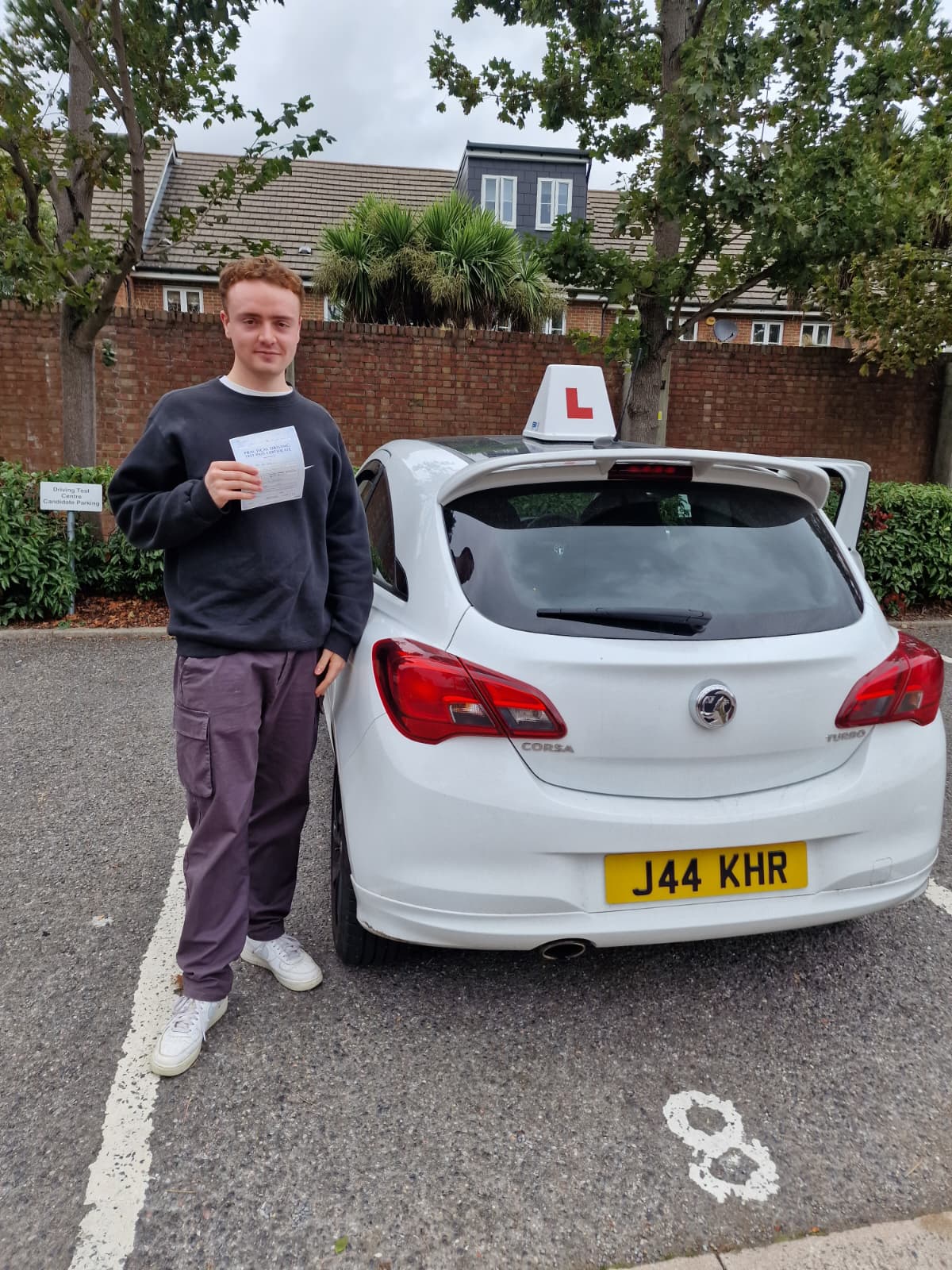 A happy learner holding their driving test pass certificate by the My First Drive car