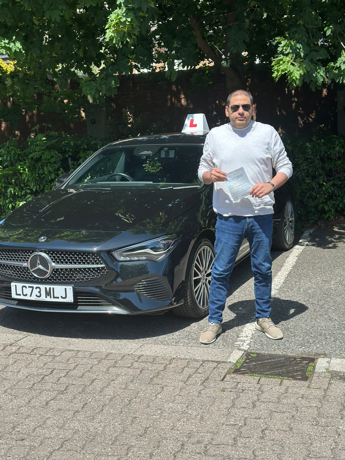 A happy learner holding their driving test pass certificate by the My First Drive car