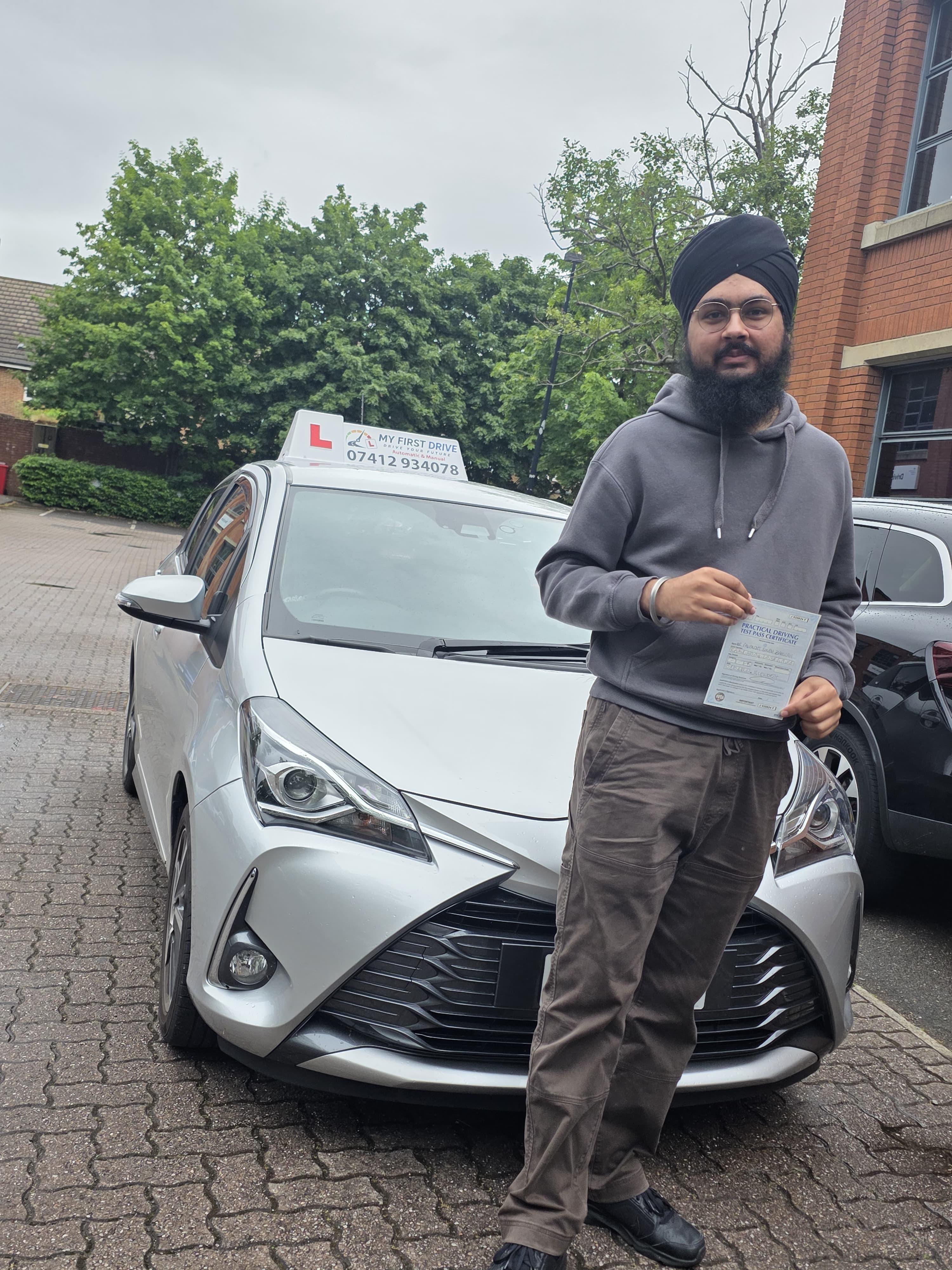 A happy learner holding their driving test pass certificate by the My First Drive car