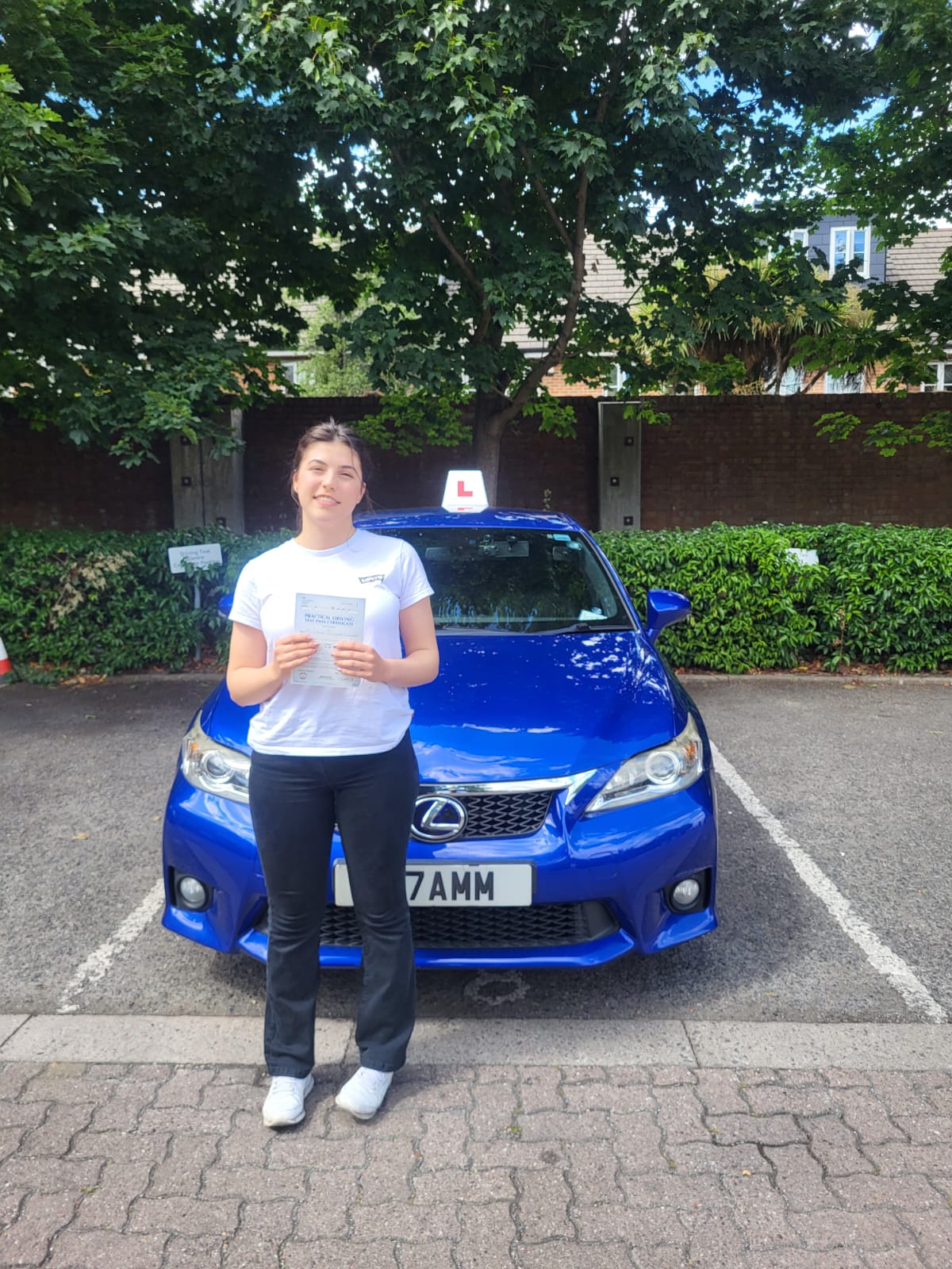A happy learner holding their driving test pass certificate by the My First Drive car