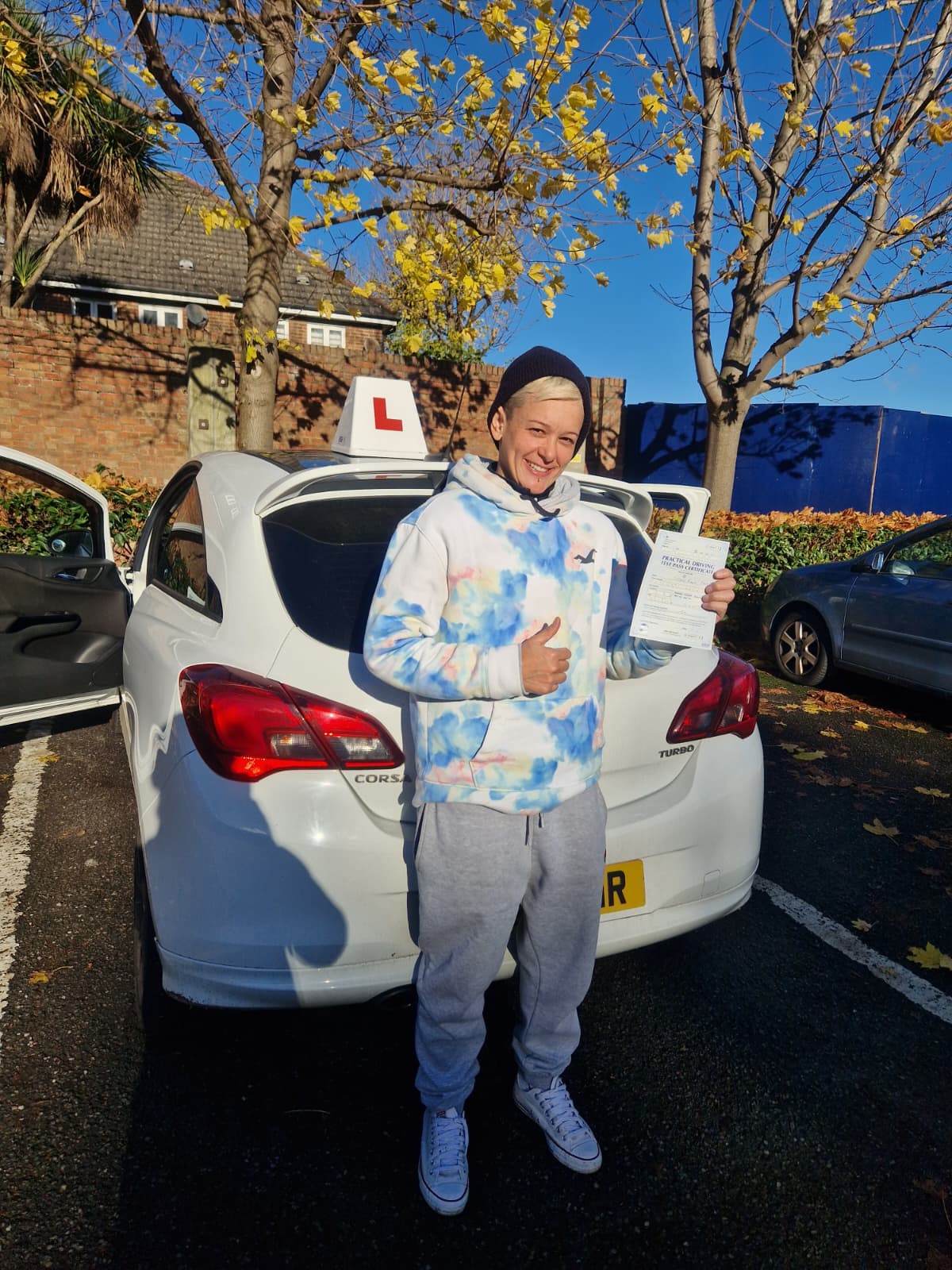 A happy learner holding their driving test pass certificate by the My First Drive car