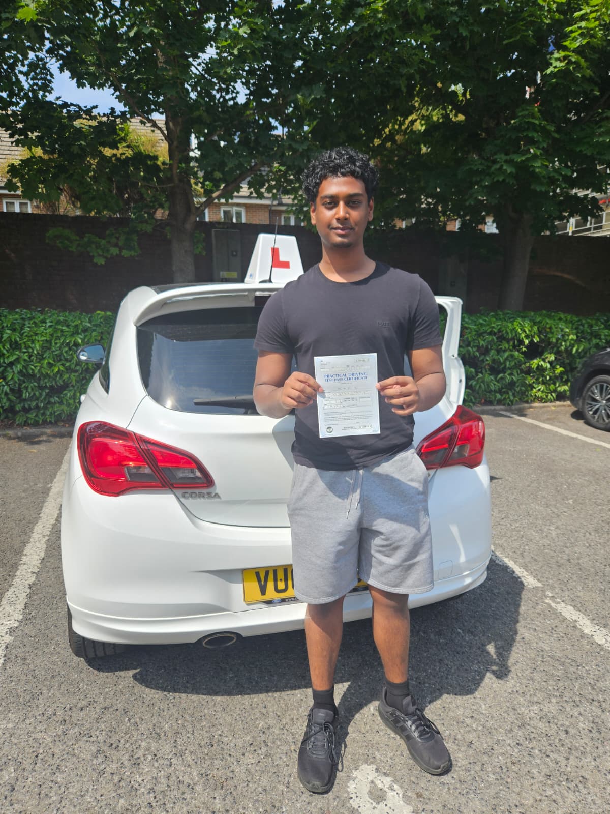 A happy learner holding their driving test pass certificate by the My First Drive car