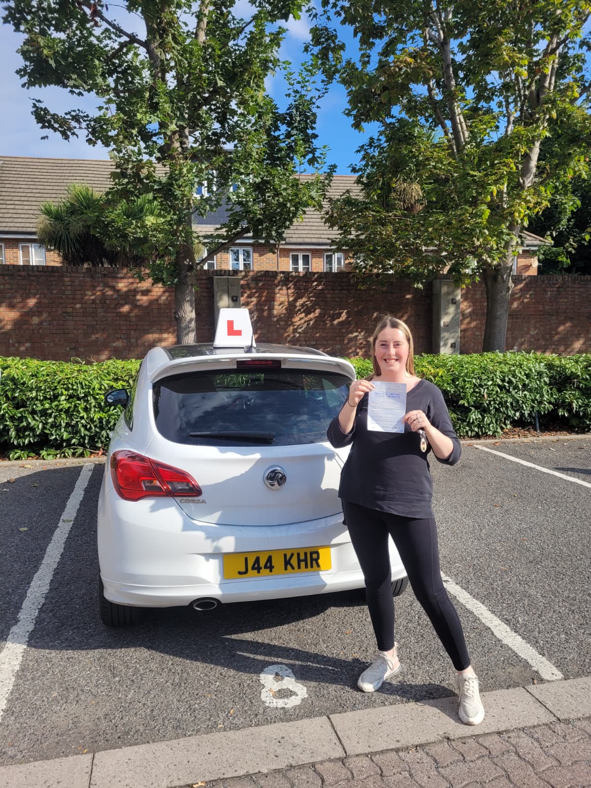 A happy learner holding their driving test pass certificate by the My First Drive car